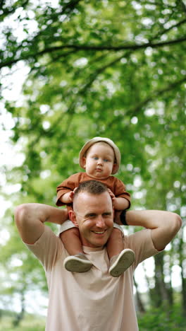 father holding his baby on shoulders. dad and little son on the walk in the nature. vertical video.