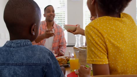 Vista-Trasera-De-Una-Familia-Negra-Feliz-Comiendo-Comida-En-La-Mesa-Del-Comedor-En-Una-Casa-Cómoda-4k