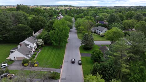 car on quiet idyllic suburb road of american neighborhood. aerial tracking shot. green trees and well-kept garden in usa. sunny day in summer.