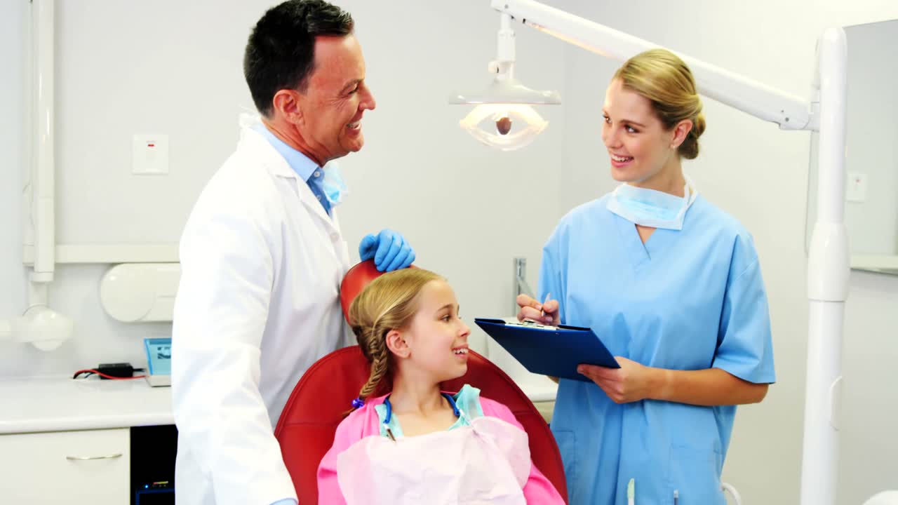 Dentist interacting with nurse while treating to girl