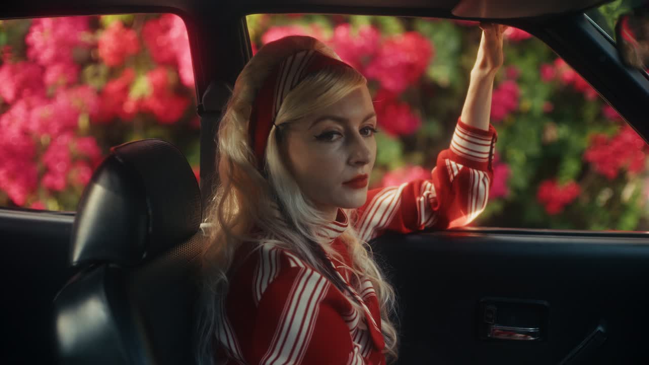 Belle femme blonde posant dans une voiture ancienne avec des fleurs roses