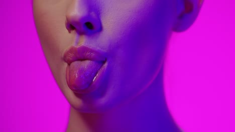 close up of a young pretty woman with beautiful red lips while sticking out her tongue with purple light in her face against purple background in slow motion