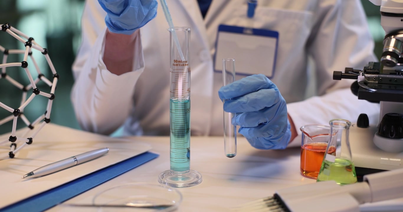 Woman scientist takes blue liquid with pipette from beaker in lab