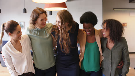 retrato de mujeres de negocios felices y diversas de pie en la oficina abrazándose y sonriendo, en cámara lenta