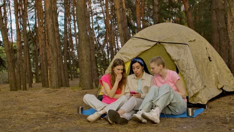 three friends looking at a phone in a forest near a tent