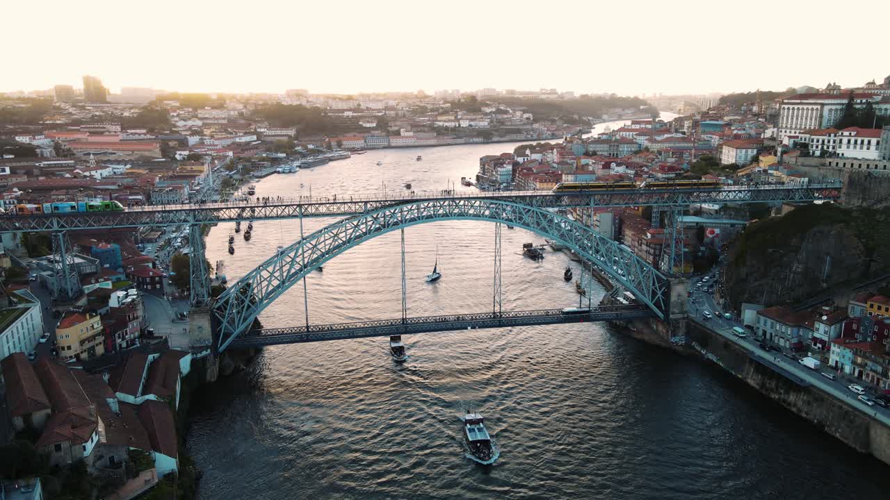 Filmagem aérea com drone ao pôr do sol da Ponte Dom Luís I no Porto, Portugal, com bondes atravessando o Rio Douro