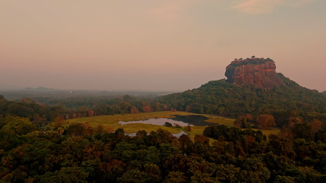 A stunning aerial clip of Sigiriya Rock at sunrise, surrounded by lush jungle and a serene lake reflecting the morning light.