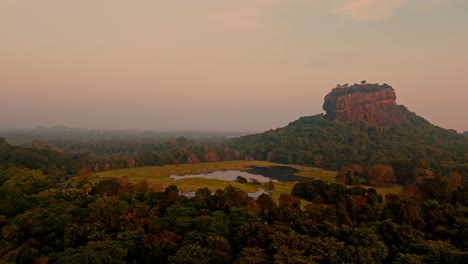 a stunning aerial clip of sigiriya rock at sunrise, surrounded by lush jungle and a serene lake reflecting the morning light.