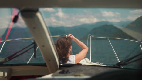 modern yacht with lady on deck sails to large mountains on summer day. woman with waving hair rides motorboat on weekend. happy time at seaside