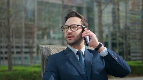 cheerful confident businessman talking on phone while relaxing in a park