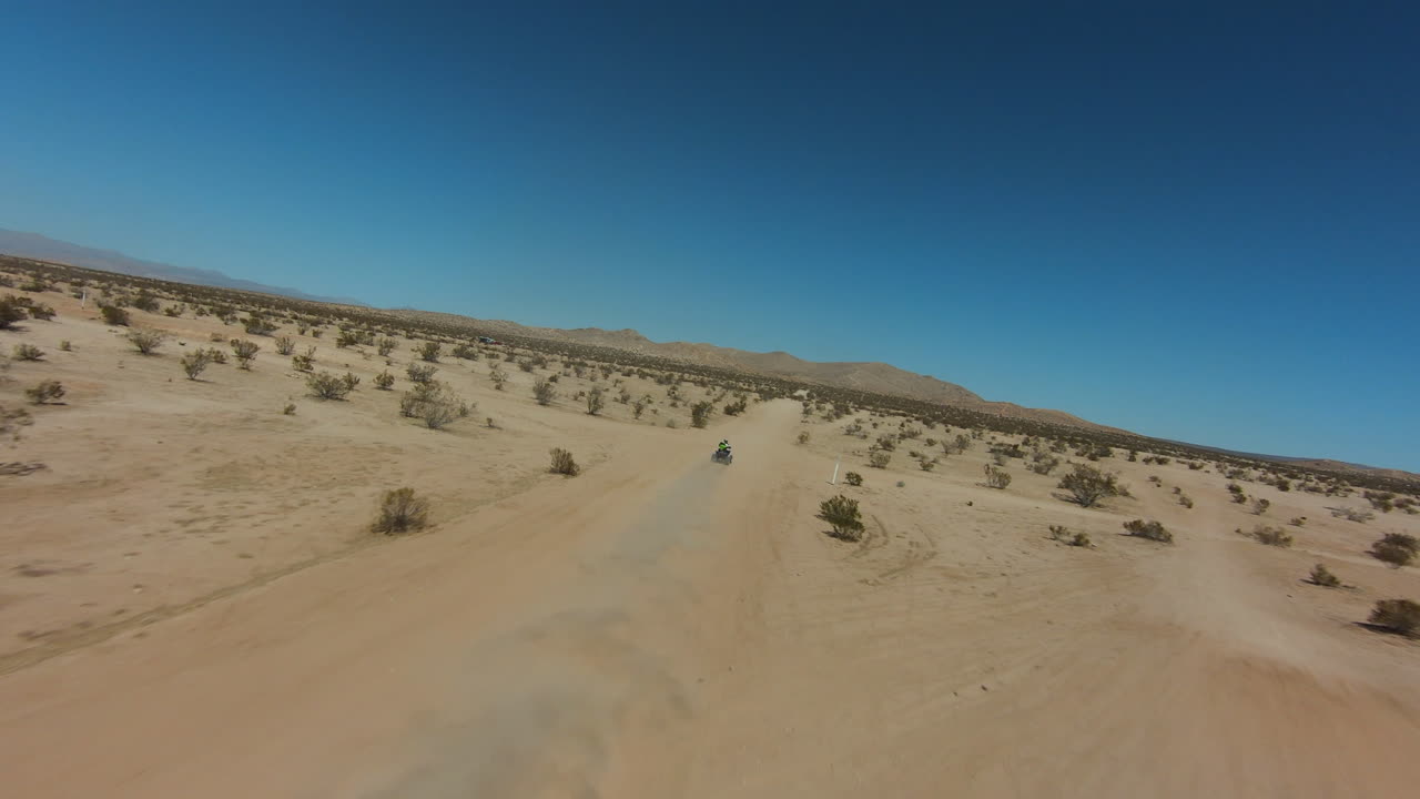 더운 날 모하비 사막의 먼지투성이 길을 따라 운전하는 4륜차 - 공중 1인칭 시점