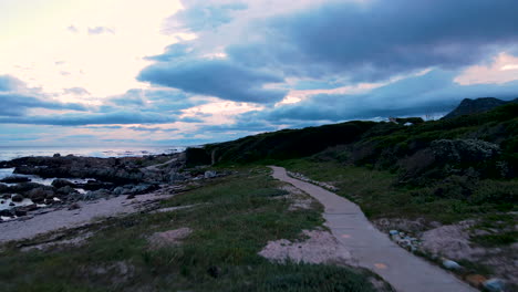 aerial dolly riser over coastal footpath along coastline, sunset cloudscape