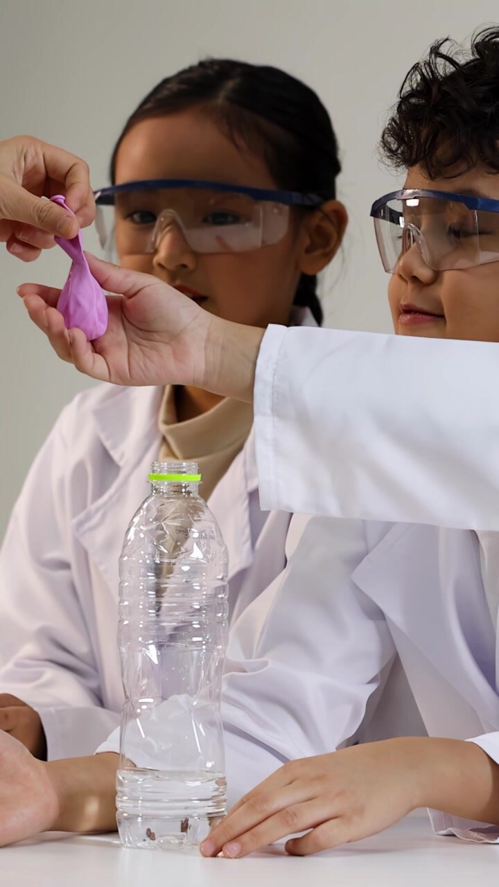 Forskellige asiatiske børn i laboratoriekittel og beskyttelsesbriller udfører et videnskabeligt eksperiment ved hjælp af plastikflasker.