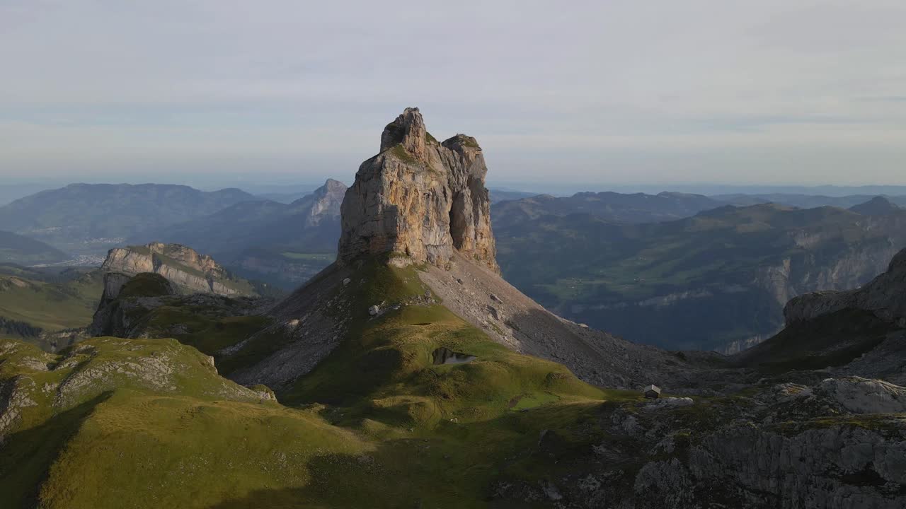 Aerial view of Gross Achslenstock, a rugged mountain peak surrounded by lush green valleys and distant hills, as a drone circles around, capturing the majestic landscape from various angles