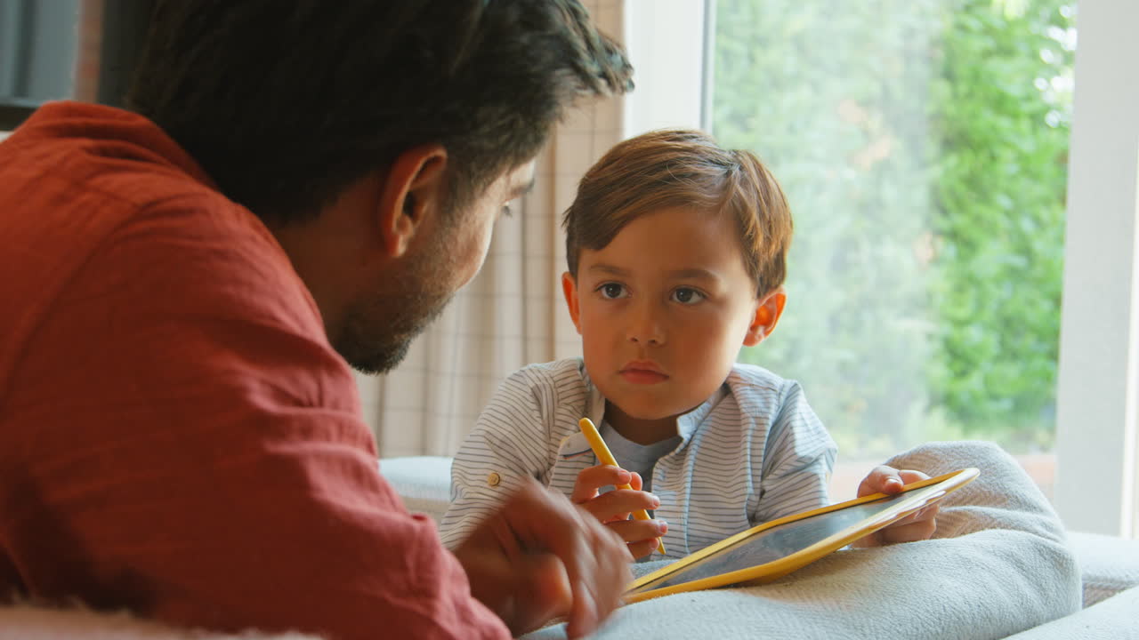 padre e hijo en casa en el sofá en la sala de estar jugando con el juego de dibujo juntos