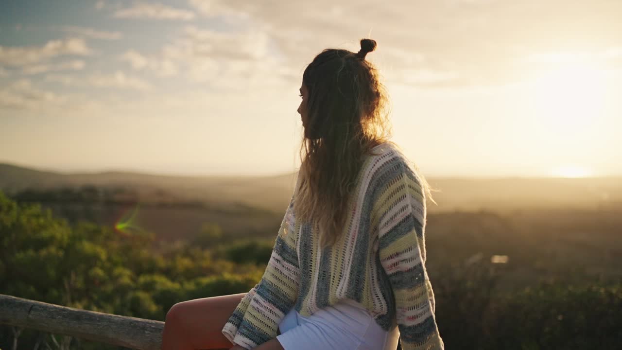 mujer joven estética posando sentada en un riel de madera con vistas al atardecer