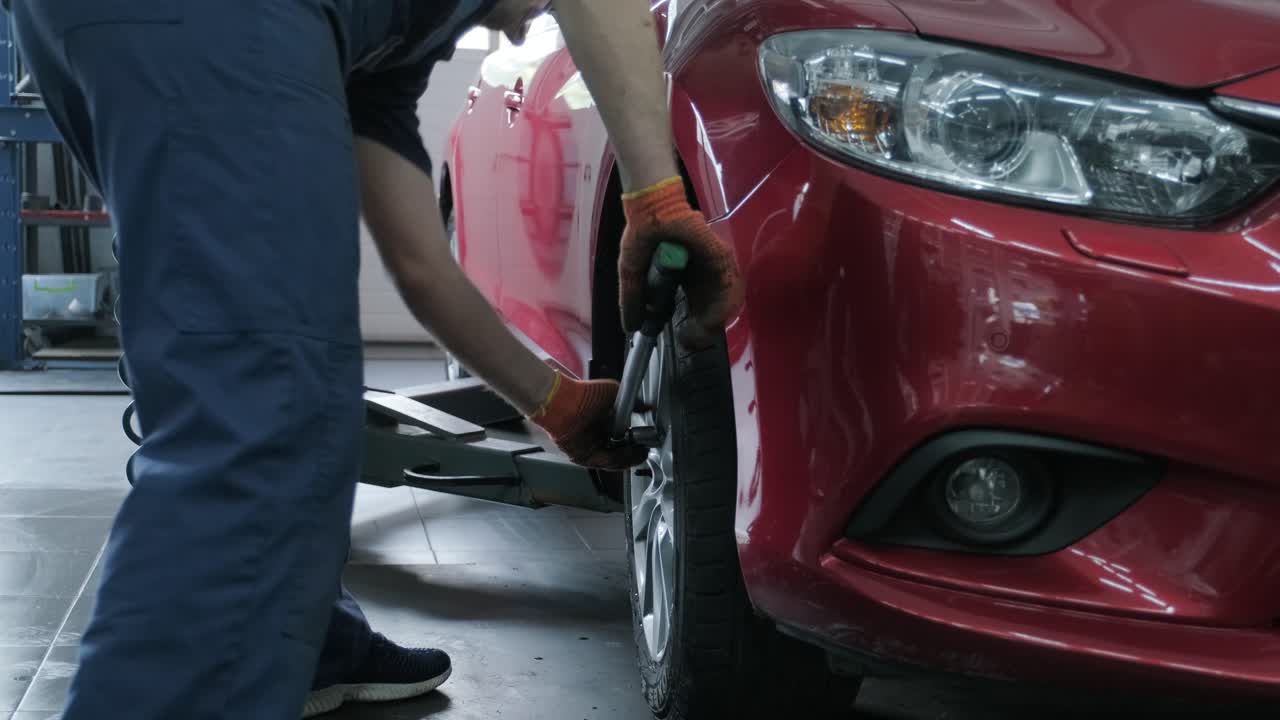 mecánico de automóviles atornillado o desenroscado de la rueda del automóvil levantado en la estación de servicio de reparación