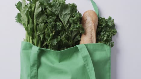 video of green canvas bag with parsley, kale and baguette, copy space on white background