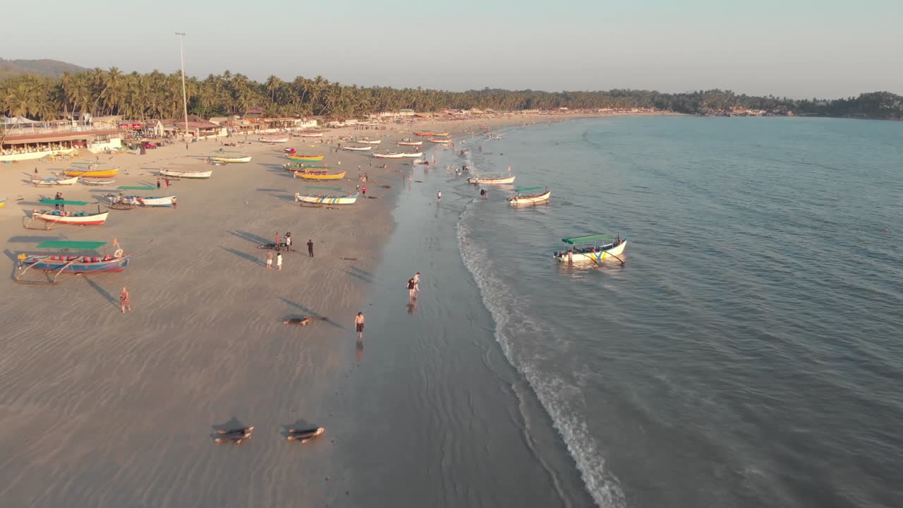 turistas paseando por las arenas doradas cerca de la costa con barcos de pesca amarrados en la playa de palolem, en goa, india - sobrevuelo aéreo