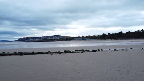 Coastal-tide-marker-aerial-view-low-dolly-right-across-moody-overcast-low-tide-seaside-beach