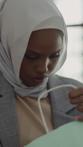 african-american lady with hijab looks inside paper shopping bag in mall hallway closeup slow motion. muslim woman does shopping. hobby and leisure