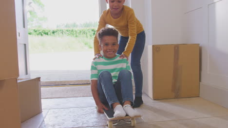 Girl-Pushing-Brother-On-Skateboard-In-Between-Boxes-On-Moving-In-Day