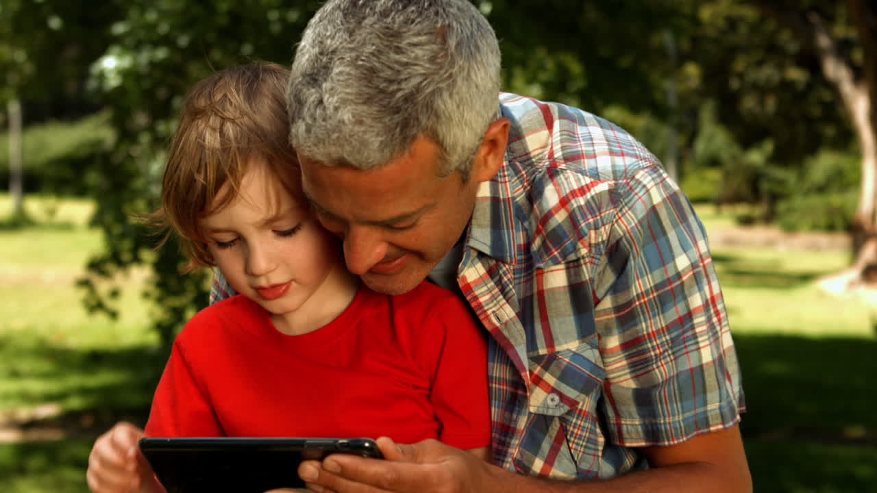 padre e hijo usando la tableta en el parque