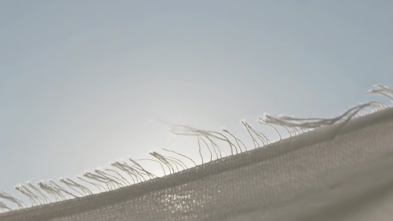 Orlo sfilacciato che ondeggia sotto un cielo azzurro pallido mentre il sole si allinea dietro le fibre, la brezza sposta le frange.