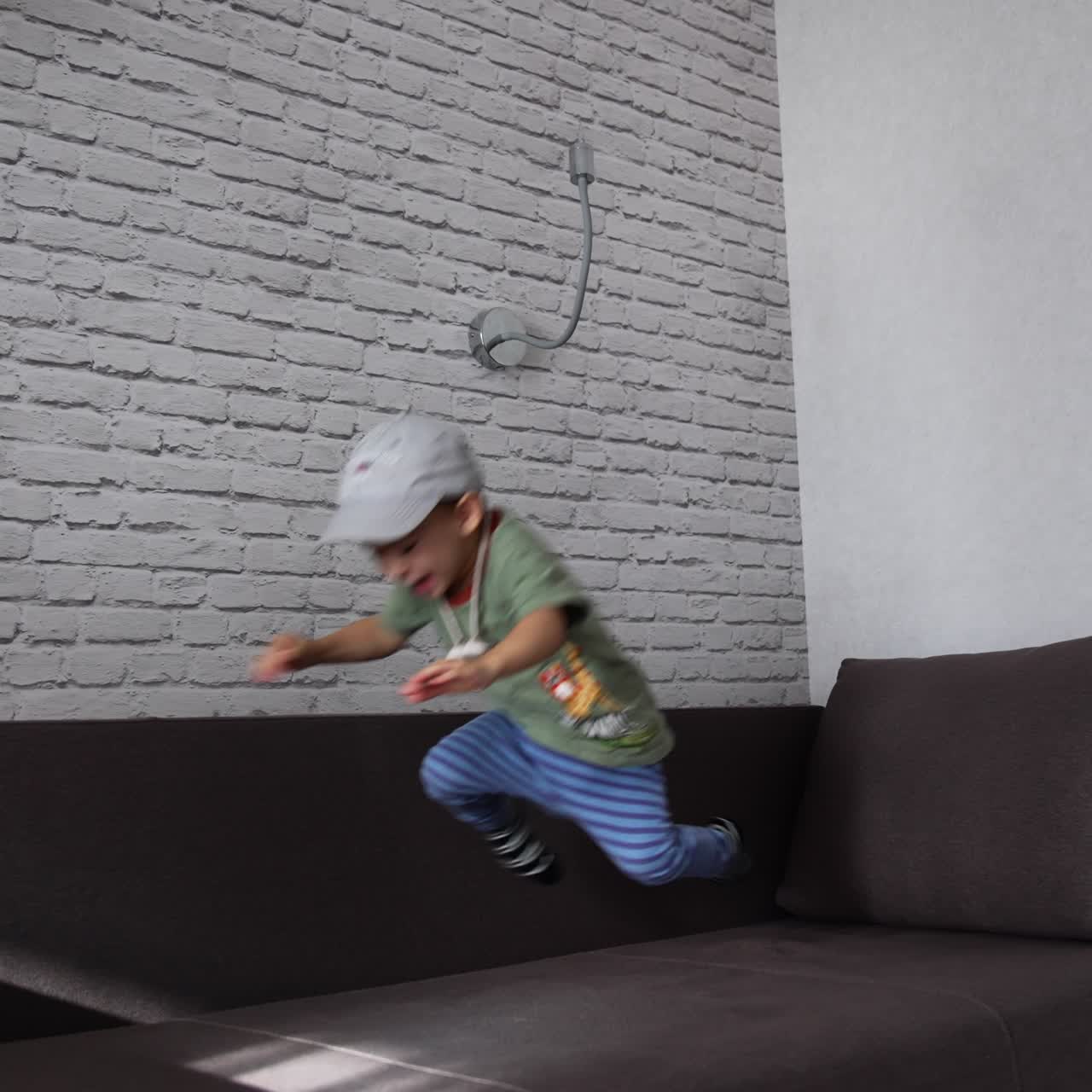 Caucasian toddler boy having fun time at home. Energetic active healthy baby boy jumping on the big sofa