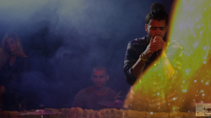 Male lead singer leaning into mic as camera shifting, flare revealing face, engaging music audience