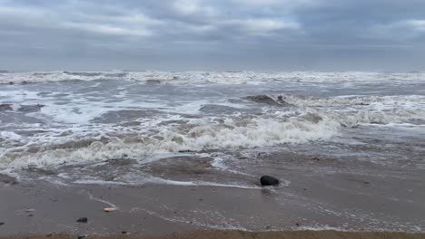 Tiefwinkelaufnahme-Der-Rauen-Nordsee,-Die-An-Einem-Bewölkten-Tag-Auf-Den-Sandstrand-Stürzt