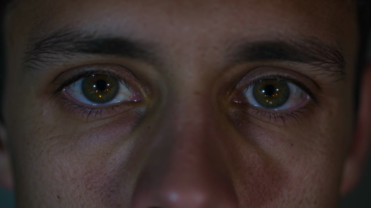 Recording camera causing adult male face shifting gaze forward in dim studio, with ring light