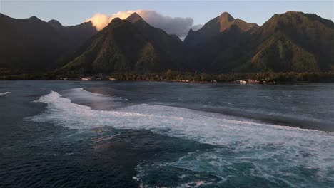 Spectacular-scene-of-Teahupoo-reef-surf-break-in-Tahiti,-French-Polynesia-with-boats-in-the-channel-and-surfers-waiting-for-waves-and-the-iconic-volcanic-mountain-peaks-in-the-back