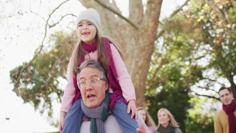 video of happy caucasian grandfather walking with smiling granddaughter on shoulders in sunny garden