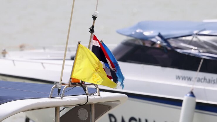 Bandiere colorate sventolano su una longtail boat a Phuket, in Thailandia, sullo sfondo sereno di acque calme e imbarcazioni ormeggiate.