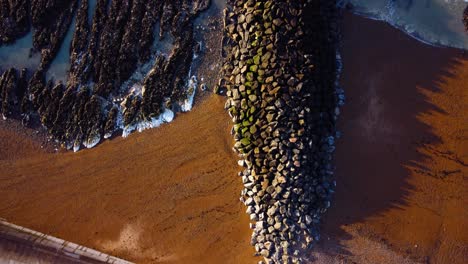 Clear-and-Bright-arial-footage-of-waves-crashing-onto-rocks-on-a-British-beach-on-a-sunny-day