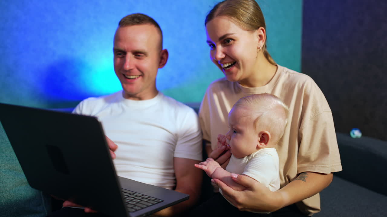 Caucasian parents showing the laptop to the tiny baby boy. Little kid looks shocked at computer.