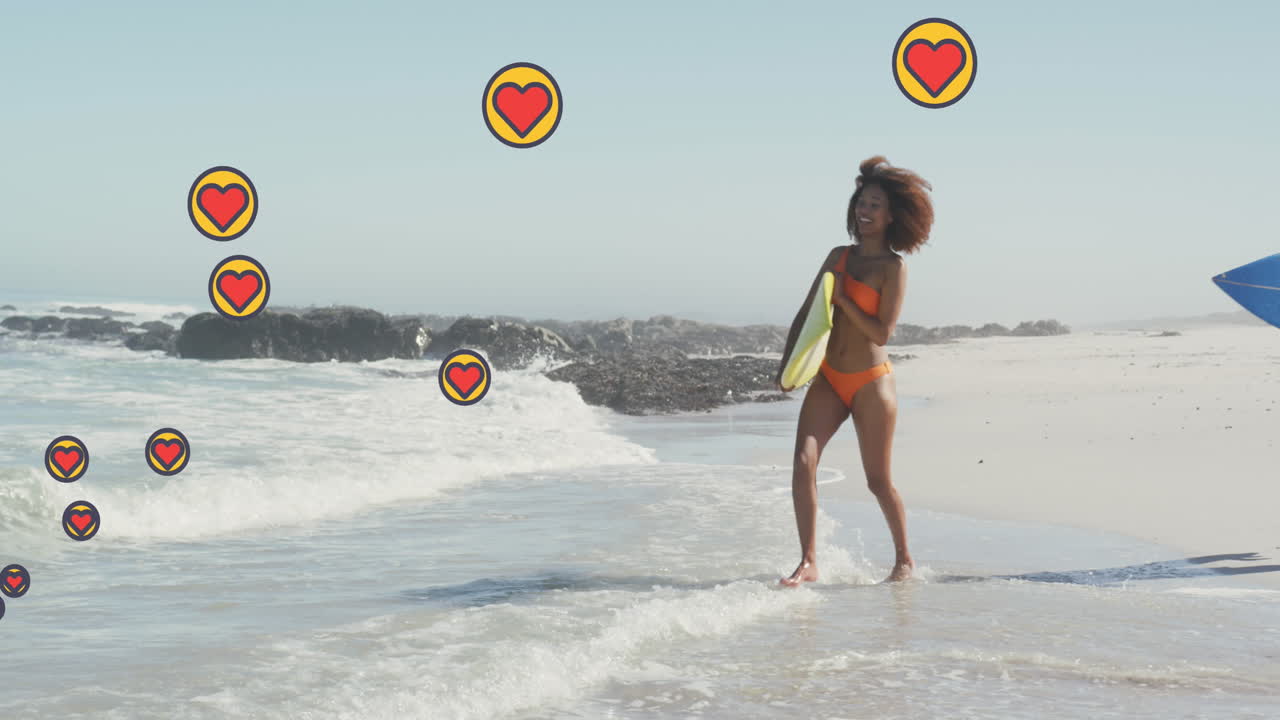 Animación de iconos digitales de corazón sobre una pareja corriendo con tablas de surf en la playa