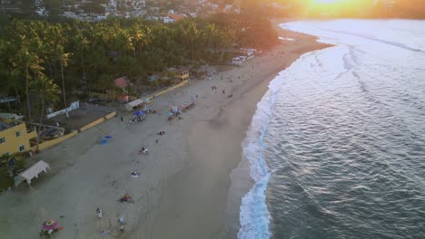 a drone flys overhead of the sayulita beach towards the setting sun in mexico