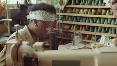 black woman cutting leather at desk in shoemaker workshop