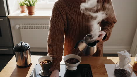 person pouring coffee with a kettle in the kitchen