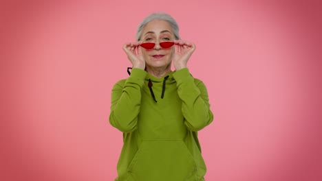 Happy-playful-elderly-stylish-granny-woman-in-sunglasses-blinking-eye,-looking-at-camera-with-smile