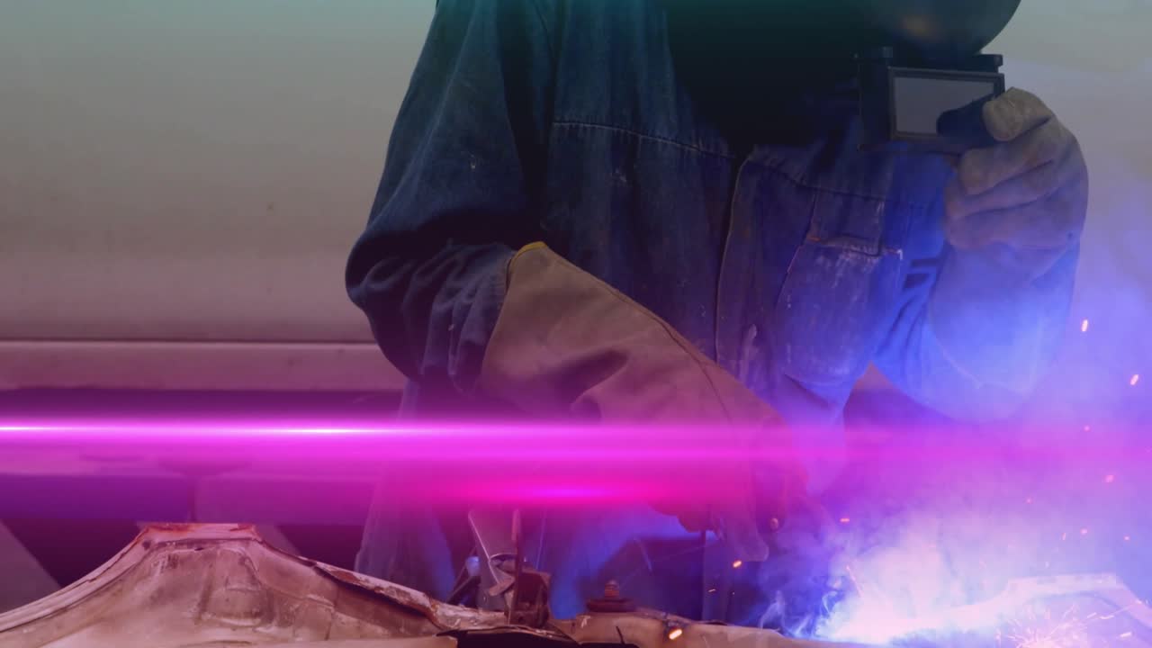 Welding tech pressing torch on panel at auto shop generating arc and orange sparks forming seam