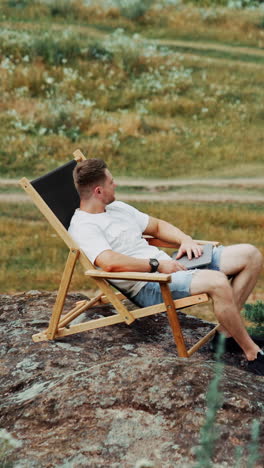 man working on laptop outdoors in a wooden chair