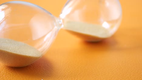 Hourglass-on-table,-sand-flowing-through-the-bulb-of-sandglass