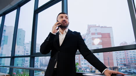 confident experienced businessman having business conversation. talking man stands near the window facing office. low angle view.