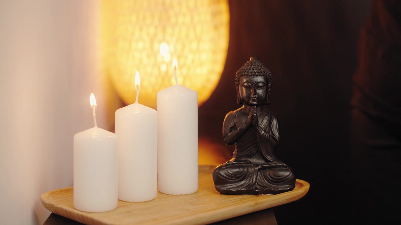 Persona che accende candele bianche accanto a una statua di Buddha