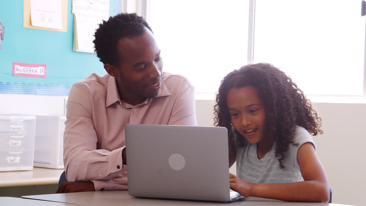 Elementary school teacher helping schoolgirl use laptop