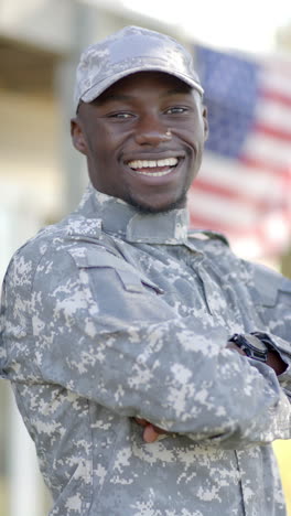 happy african american male soldier standing with flag in background on sunny day, slow motion