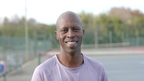 portrait of happy african american male tennis player smiling at outdoor court, slow motion